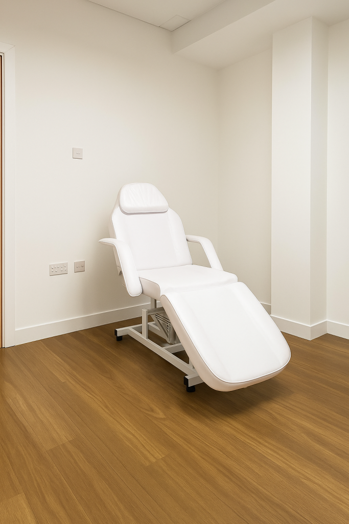 Clean and professional clinical treatment room with a reclining chair on wooden flooring and white walls.