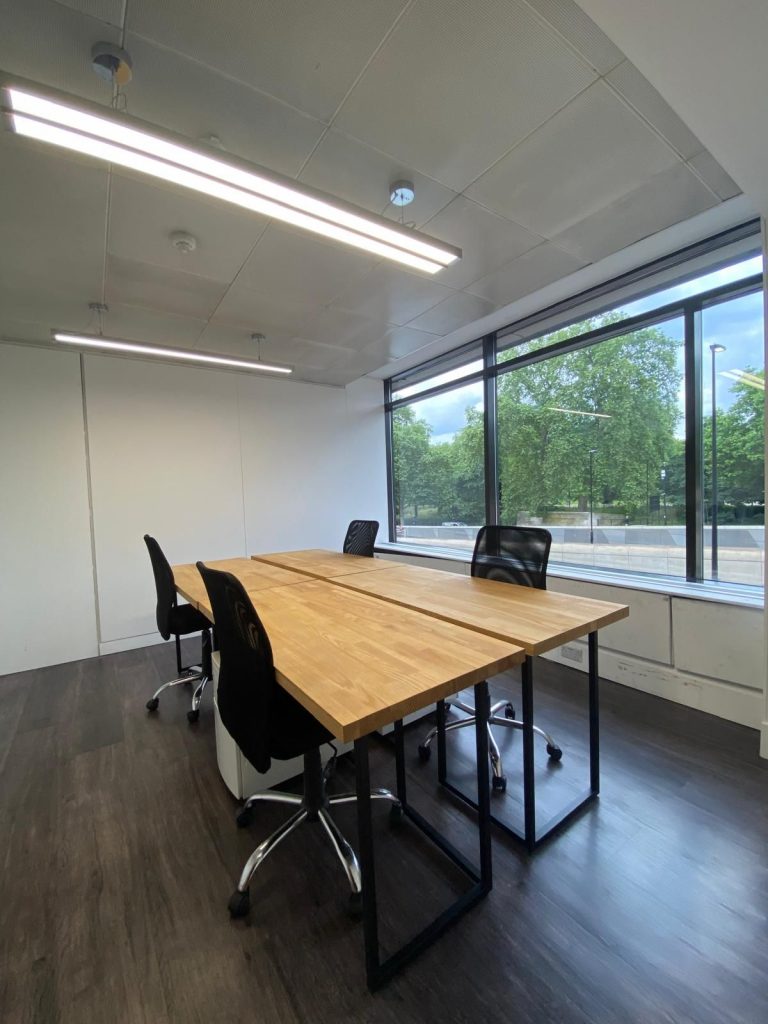 Modern office in Hyde Park Corner with desks, chairs, and large window overlooking green space.