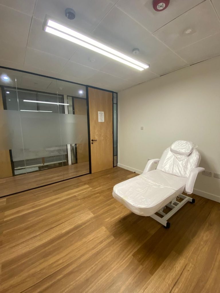 Modern clinical room with a white adjustable therapy chair and frosted glass partition.