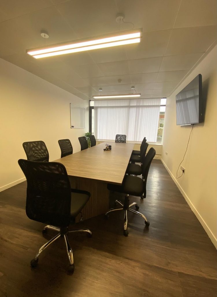 Modern meeting room with large wooden table, office chairs, and natural light from a full-length window at 21 Knightsbridge.